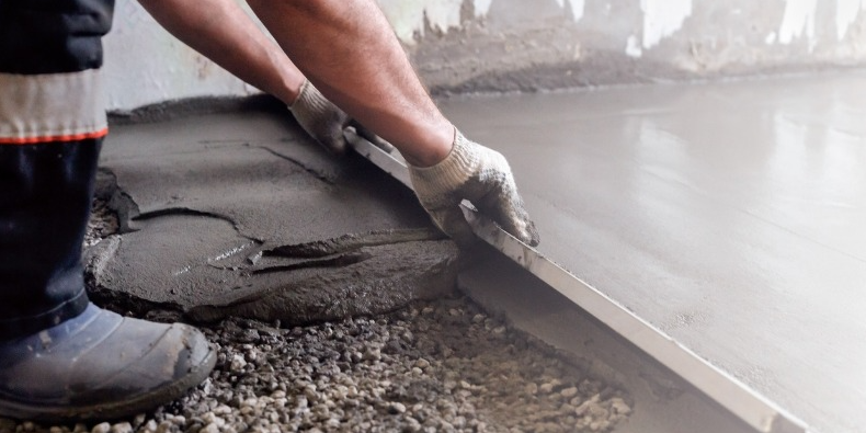 Tradesperson levelling a concrete floor screed, relating to replacing floor heating