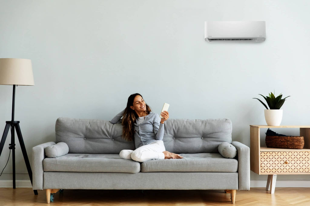 Woman relaxing on a sofa below a wall mounted split system air conditioner